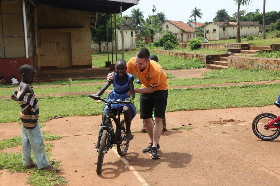 Collega van 12GO Biking helpt een meisje op weg op de fiets tijdens een reis van Bikes4Africa